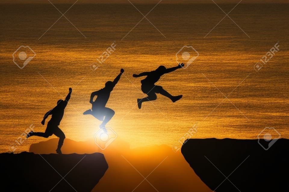 Men jump cliff sun light over silhouette