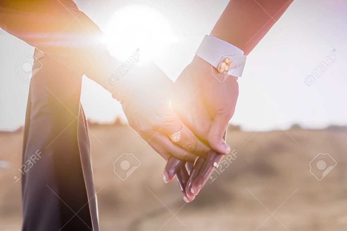 Segurando as mãos com anéis de casamento no fundo da luz solar