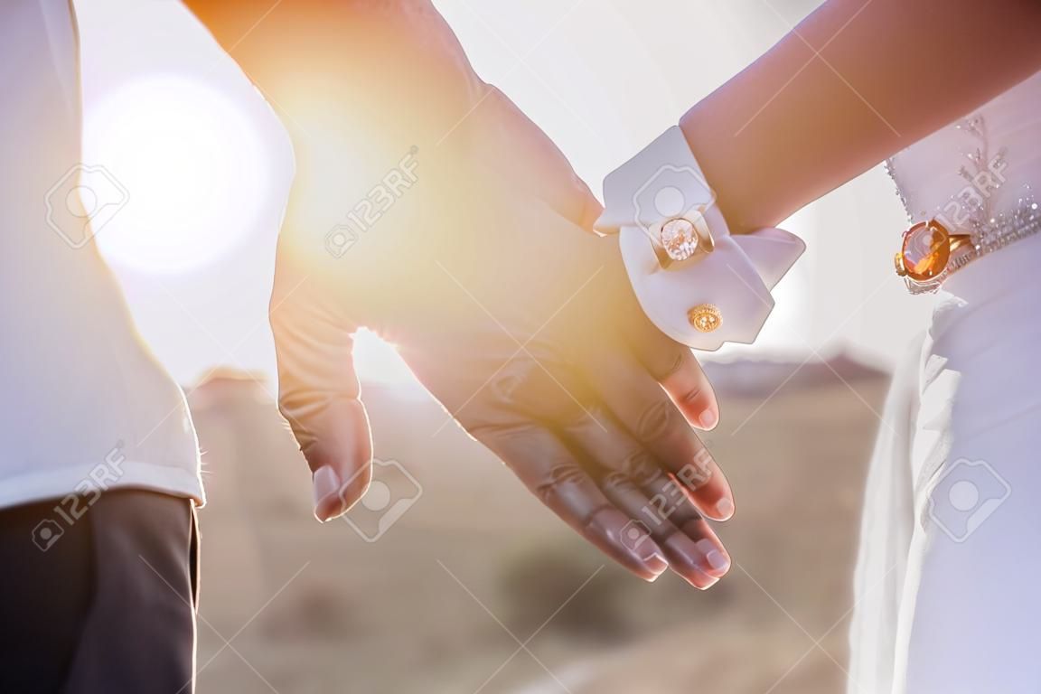 Держась за руки с обручальными кольцами на фоне солнечных лучей