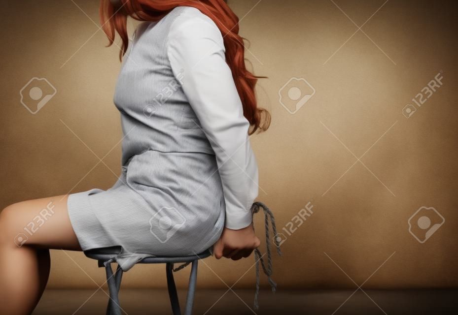 Le mani della donna legate con il concetto di rapimento della sedia di seduta della corda
