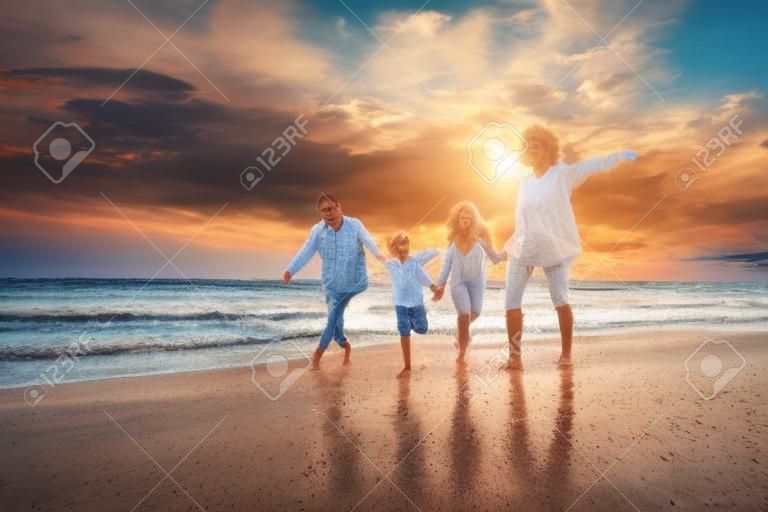 Vacances d'été tropicales, famille heureuse s'amusant à courir sur une plage de sable au coucher du soleil, père, mère, enfants fils et fille famille de quatre personnes se tenant la main ensemble marchant sur la plage