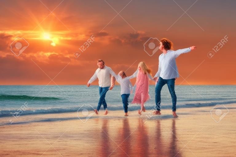 Tropical summer vacations, Happy family having fun running on a sandy beach at sunset time, People of father, mother, children son and daughter family of four holding hands together walking on beach