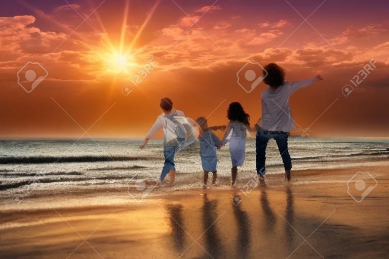 Férias de verão tropicais, família feliz que se divertem correndo em uma praia de areia na hora do por do sol, pessoas do pai, da mãe, dos filhos filho e da filha família de quatro de mãos dadas junto andando na praia