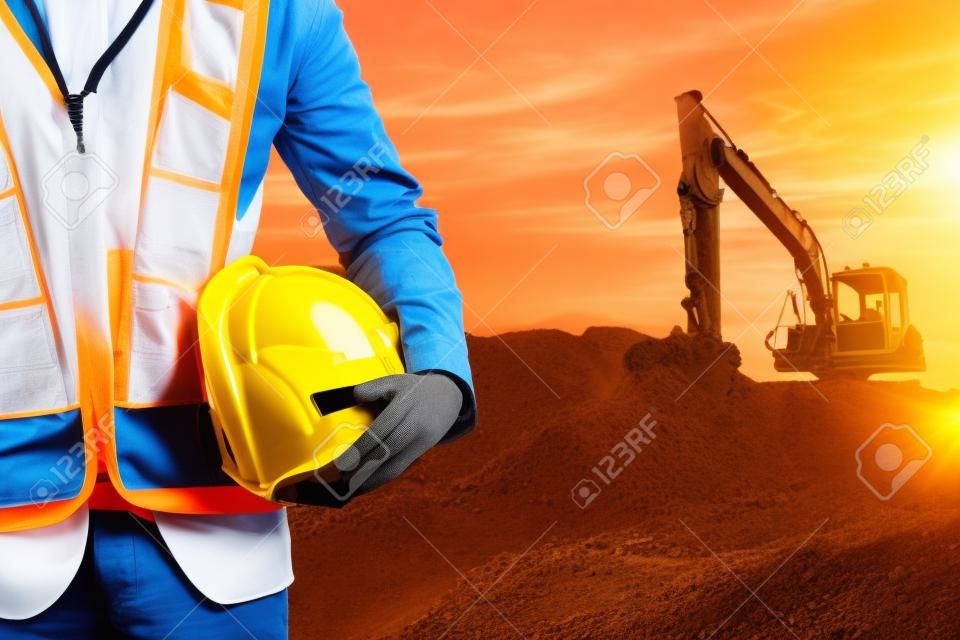 エンジニアや日没時間に建設現場で掘削機のマシンとヘルメットを保持しているセーフティ ・ オフィサーは、背景です。