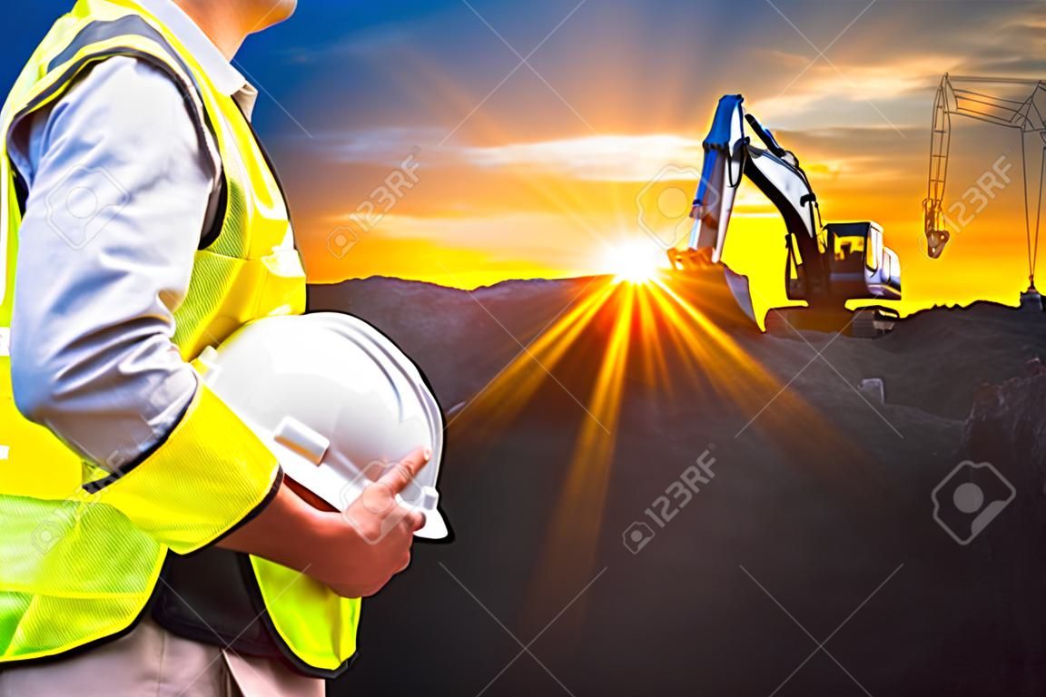 エンジニアや日没時間に建設現場で掘削機のマシンとヘルメットを保持しているセーフティ ・ オフィサーは、背景です。