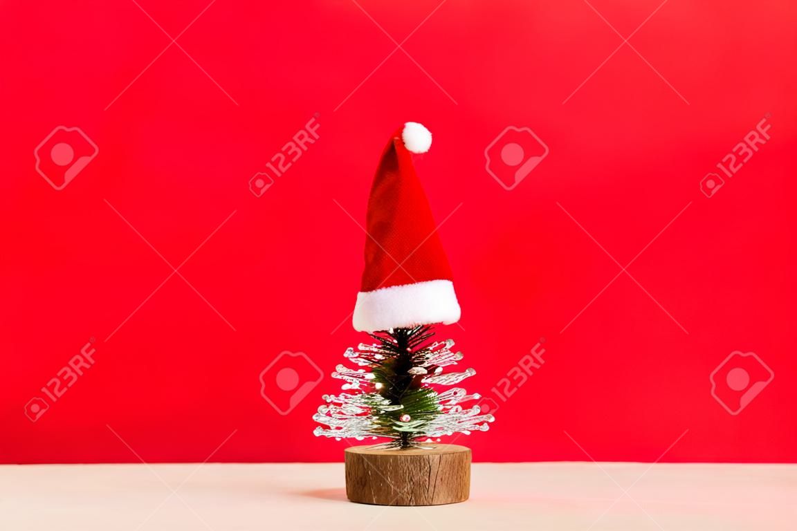 Ein kleiner Weihnachtsbaum mit Weihnachtsmütze auf farbigem Hintergrund, Neujahrsdekoration mit Kopierraum