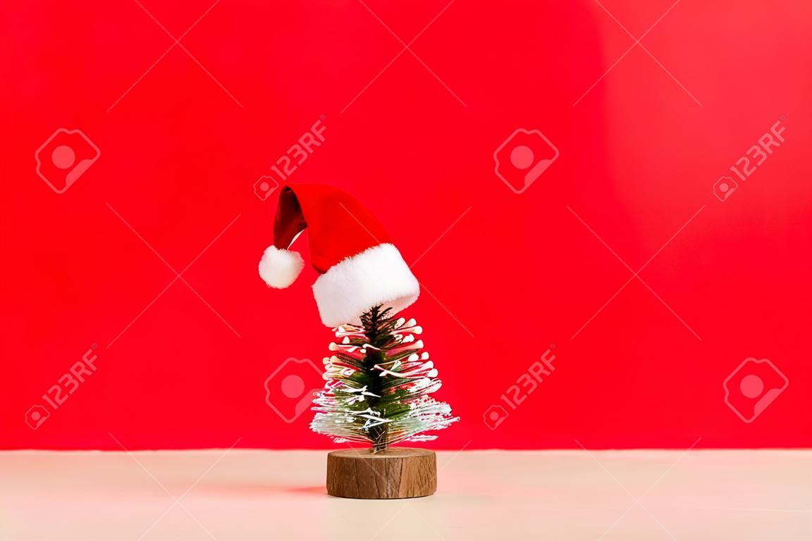 Uma pequena árvore de Natal com chapéu de Papai Noel em fundo colorido. Decoração de ano novo com espaço de cópia.