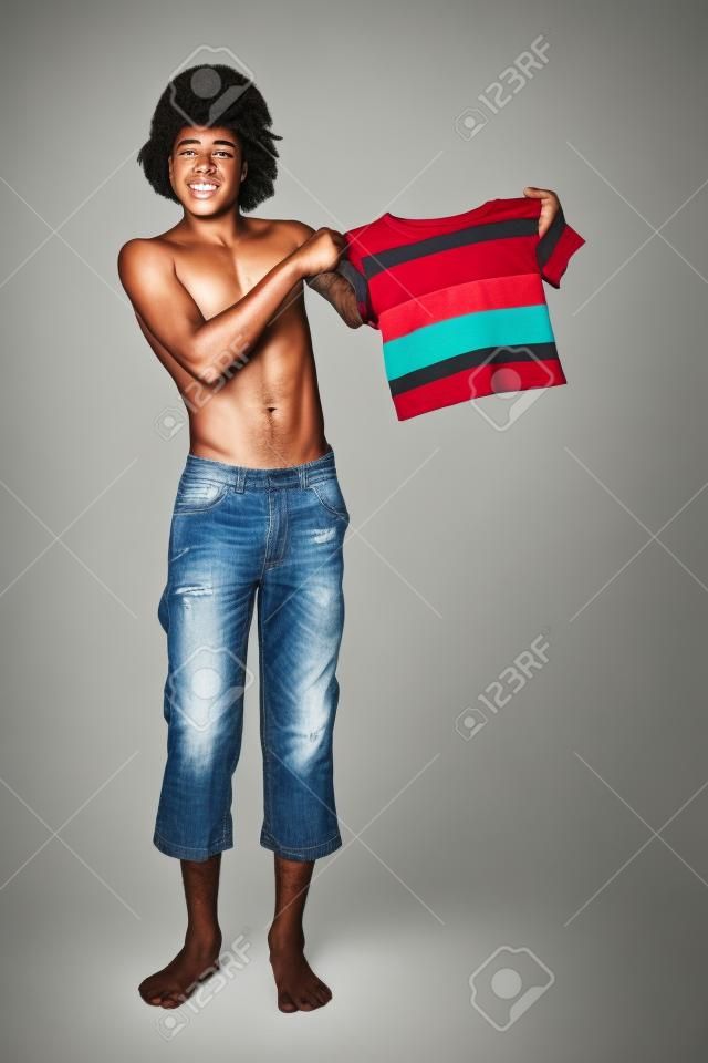 A teenager holds up a shirt that he has obviously outgrown. His pants are way too short