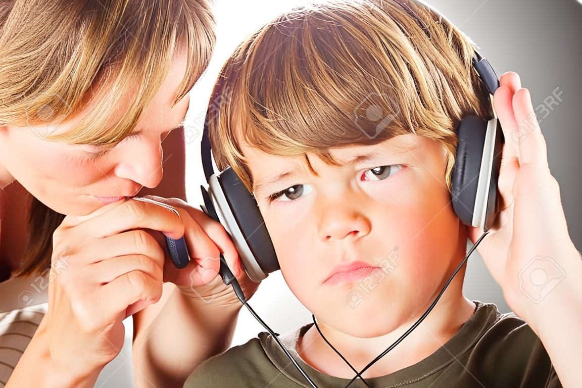 A mother pulls the headphone off of her son to tell him something