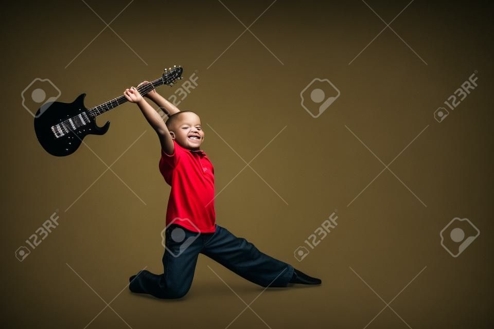 Young boy with black electric guitar raised up over his head as if he's going to smash it.