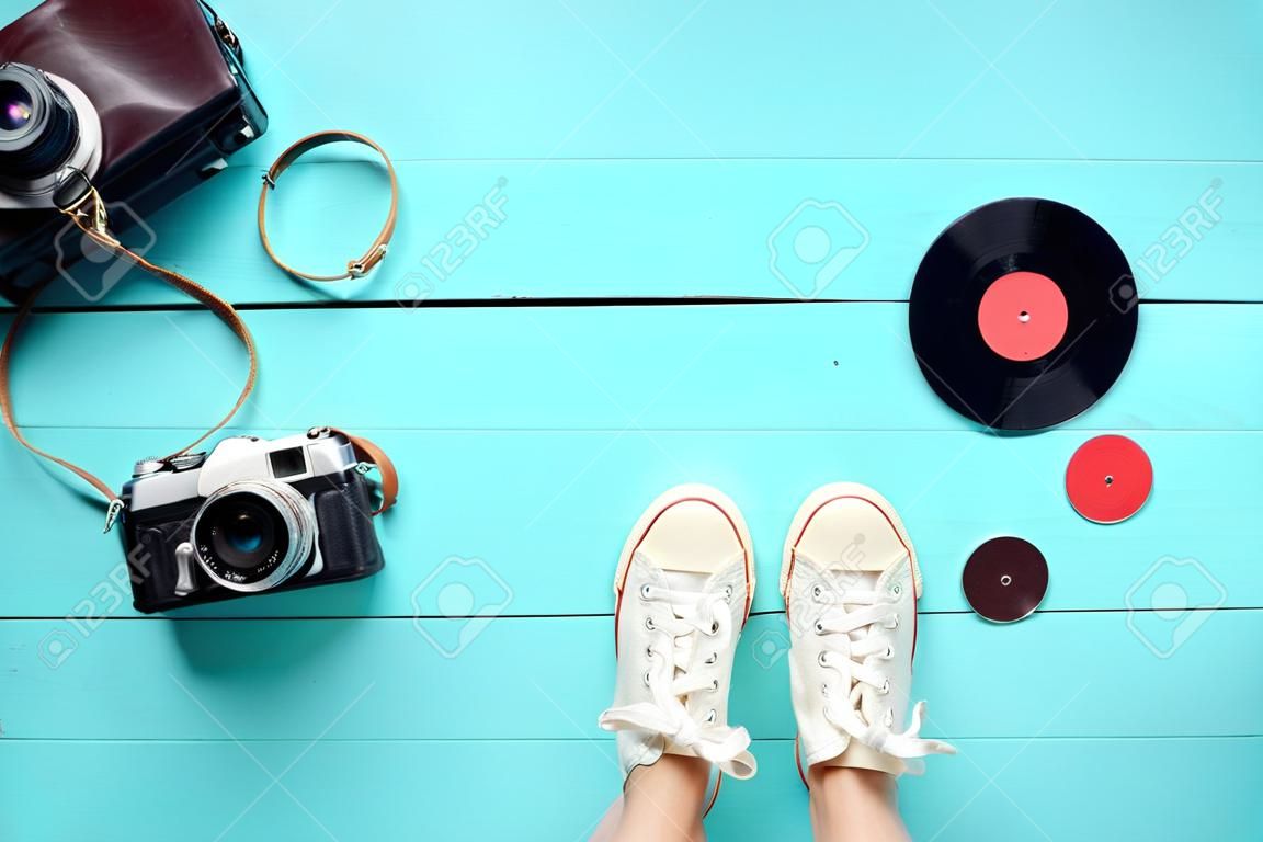 Retro still life. Old fashioned sneakers, vinyl record and vintage film camera on blue wooden background. Top view. Flat lay