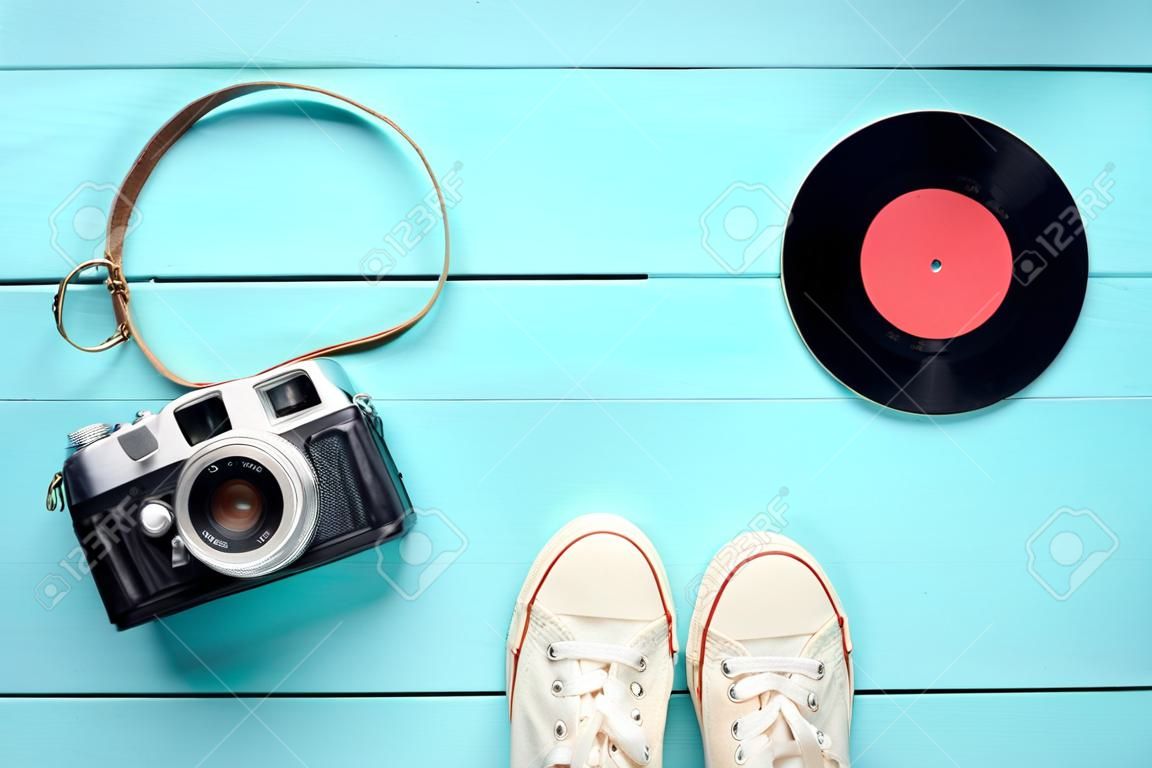 Retro still life. Old fashioned sneakers, vinyl record and vintage film camera on blue wooden background. Top view. Flat lay