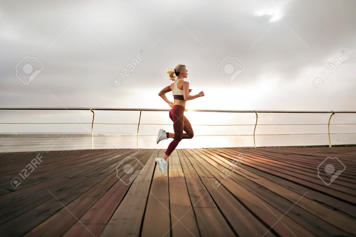 Course du matin. Une jeune femme athlétique en vêtements de sport court sur la plage au lever du soleil. Entraînement en plein air. Mode de vie sain