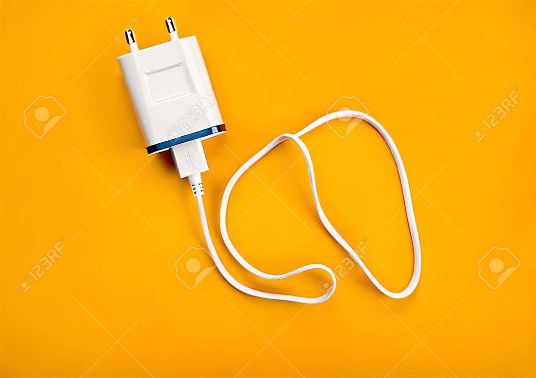 Charger with cable on yellow background. Top view