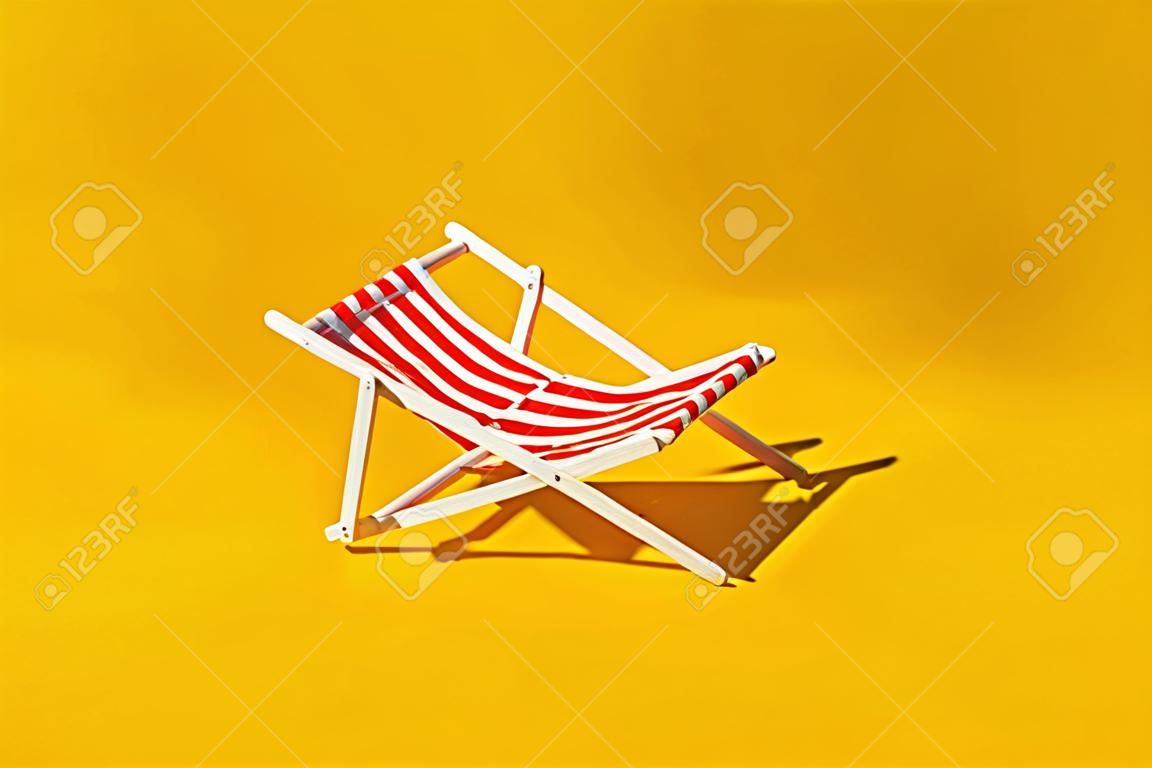 Mini beach deck chair on yellow background with shadow. Sunlight. Symbol of beach holidays, resort. Relax, Summer minimal concept.