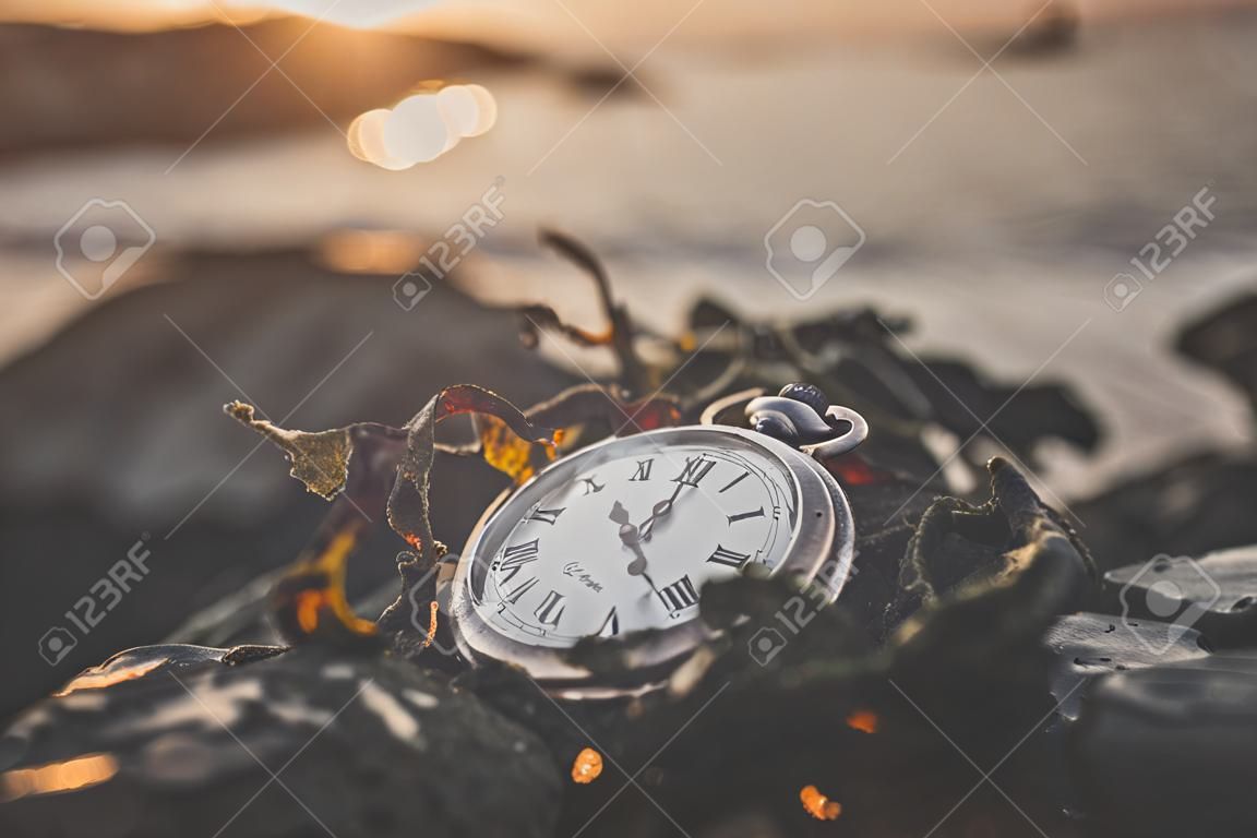 Relógio velho em uma rocha pelo oceano no nascer do sol do verão coberto com algas marinhas