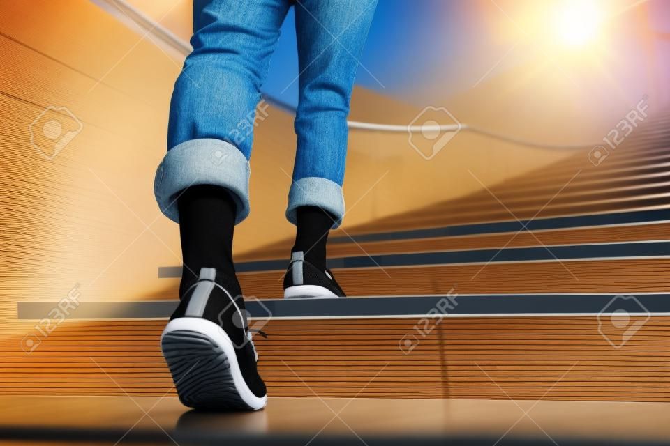 Mulher adulta nova que anda acima das escadas com fundo do esporte do sol.