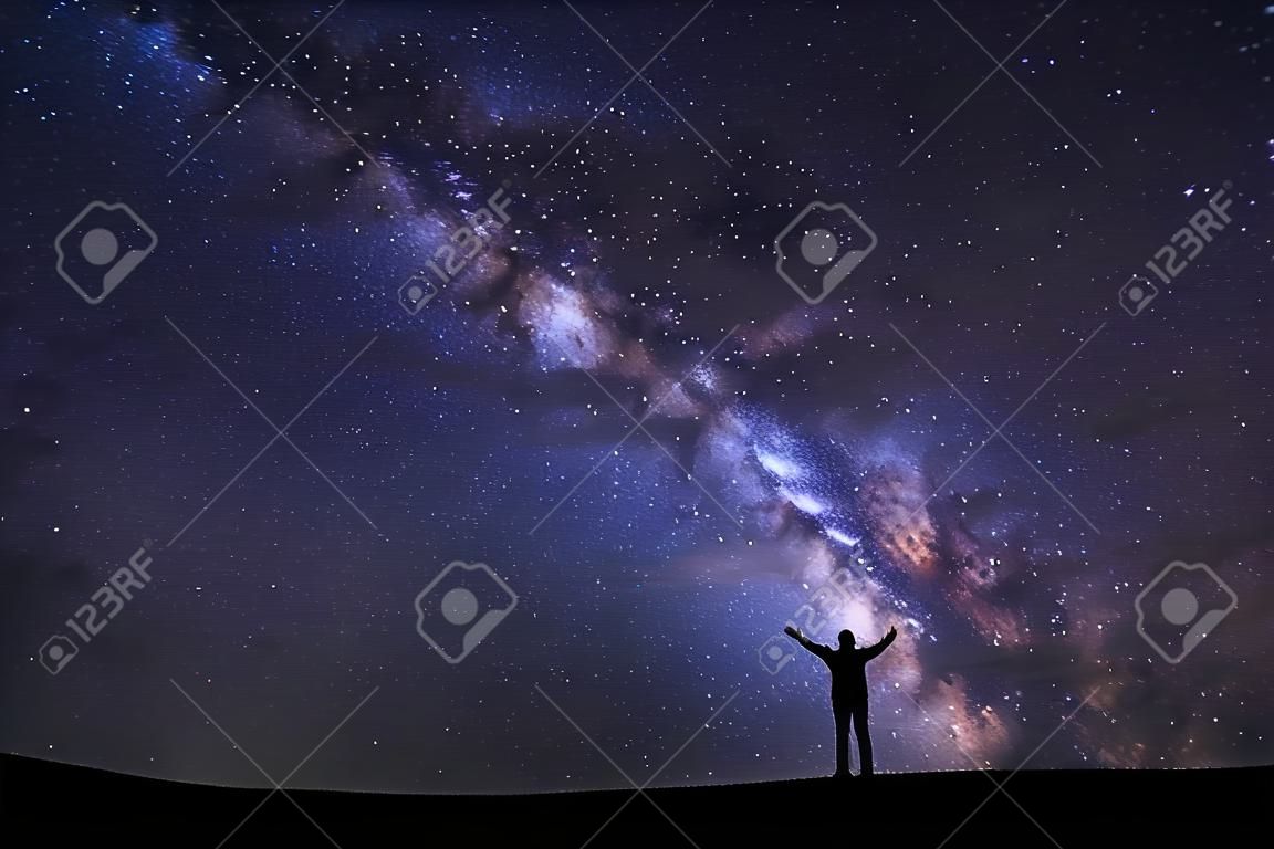 landscape with milky way, Night sky with stars and silhouette of a standing sporty man with raised up arms on high mountain.
