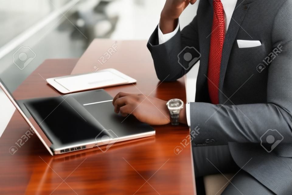 A beautiful stylish African American businesswoman wearing a suit uses his laptop while working.