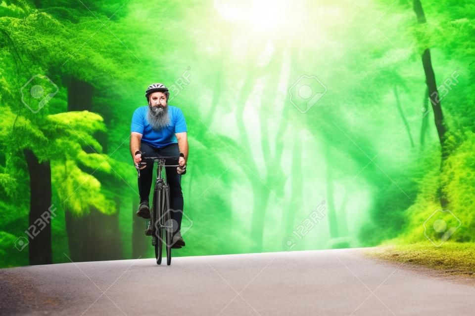 Bebaarde man. Fietser op een fiets is op de asfaltweg in het bos op zonnige dag.