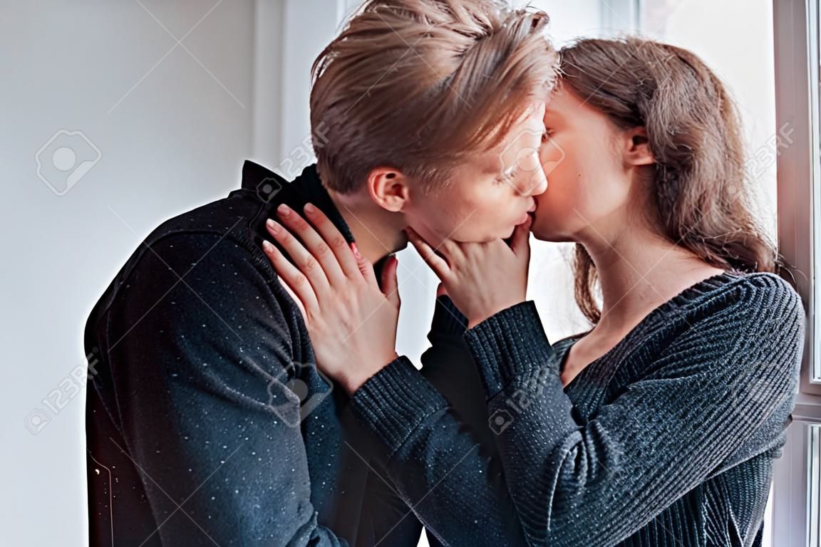 Casal jovem bonito beijando-se dentro de casa perto da janela.