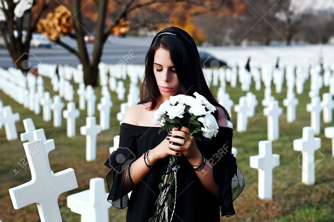 Young woman in black clothes visiting cemetery with many white crosses. Conception of funeral and death
