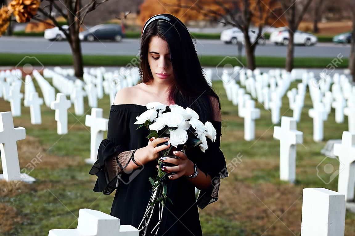 Young woman in black clothes visiting cemetery with many white crosses. Conception of funeral and death