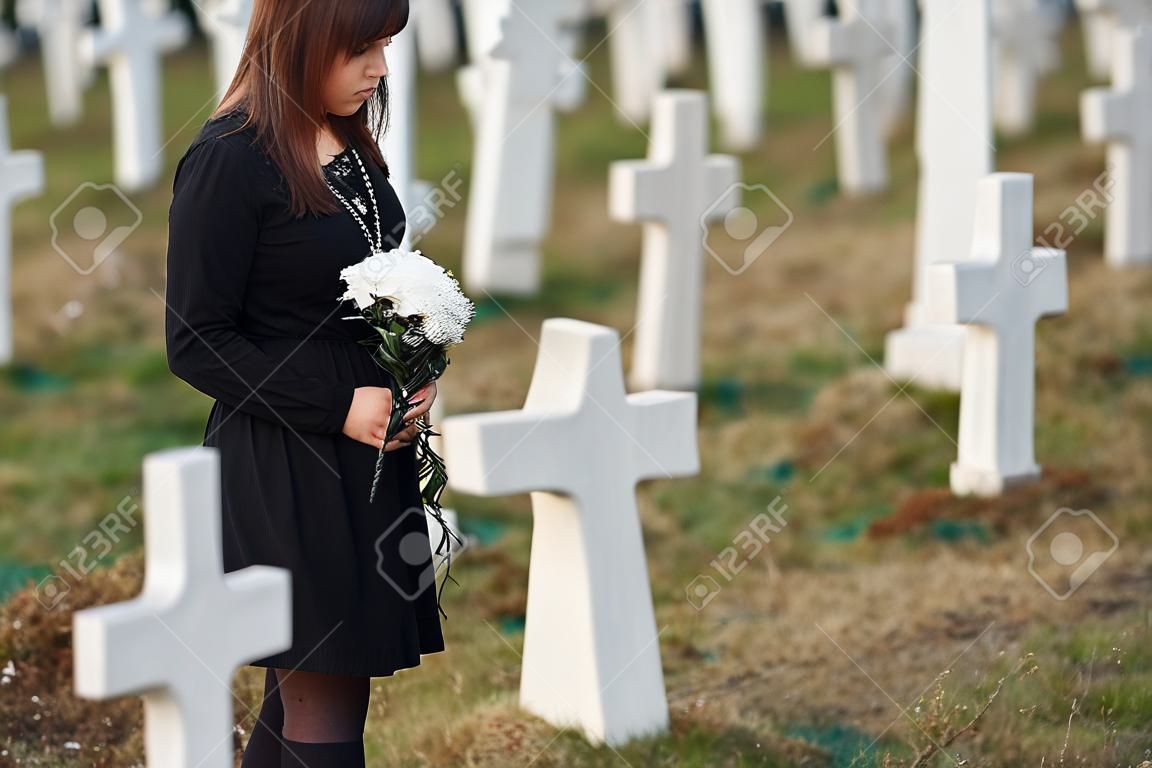 Vista particellare giovane donna in abiti neri che visita il cimitero con molte croci bianche concezione del funerale e della morte