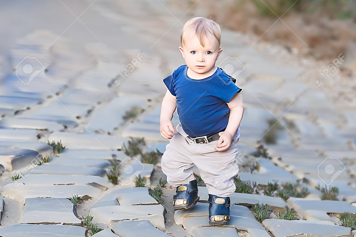 Feliz niño lindo en la vieja calzada. La sonrisa de un niño al aire libre en carretera pavimentada con piedra en la puesta del sol