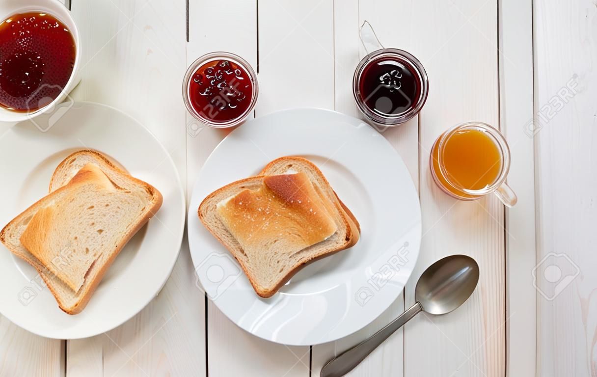 Een witte kop zwarte thee met broodjes of toast met aardbei, bessen en abrikozengelei of jam op witte houten tafel, bovenzicht, vlak leggen, Ontbijt concept met kopieerruimte