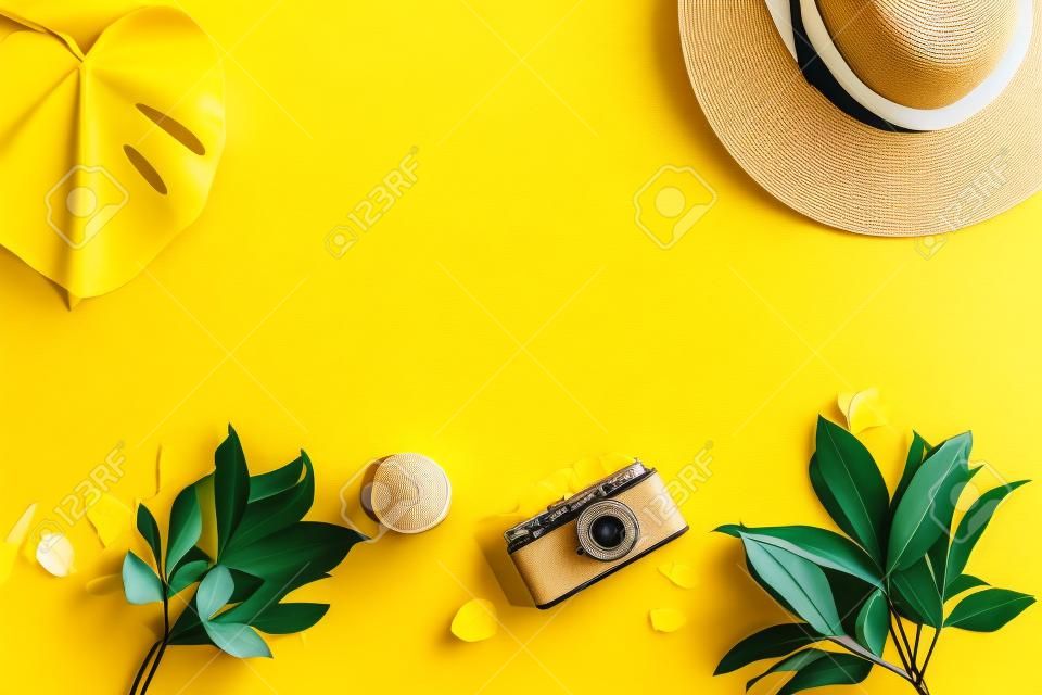 Top view and flat lay of yellow background for summer vacation, photo camera, hat, palm leaf. Copy space.