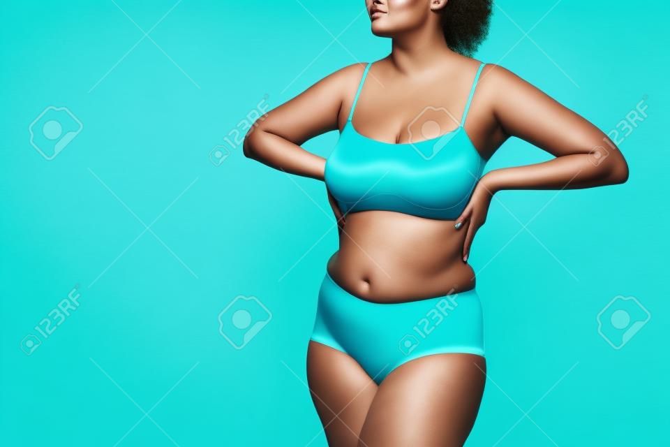 Plus-Size-Model in blauer Unterwäsche auf türkisfarbenem Hintergrund, körperbetontes Konzept