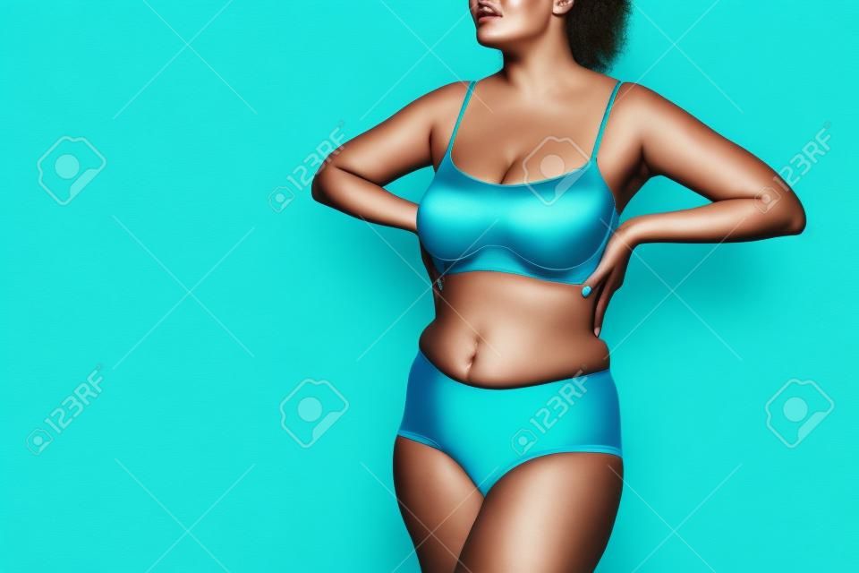 Modelo de talla grande en ropa interior azul sobre fondo turquesa, concepto positivo para el cuerpo