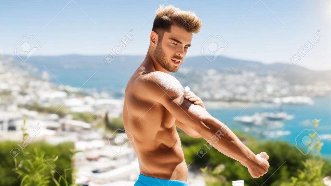 Giovane uomo senza camicia che indossa una crema solare, uomo muscoloso che indossa un costume da bagno pronto a prendere il sole sulla terrazza
