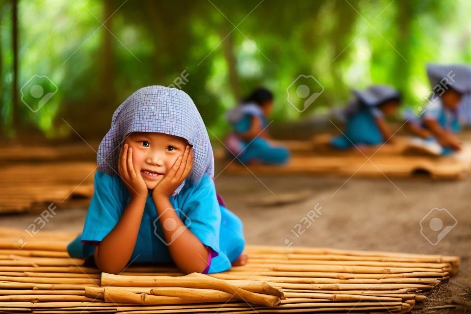 Mädchen in Schuluniform auf einer Bambusmatte im ländlichen Thailand.