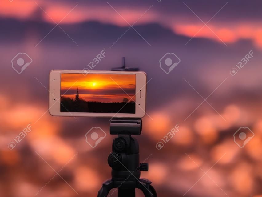 Smartphone close-up tirar uma foto da paisagem e timelapse de vídeo no tripé stand no pôr do sol.