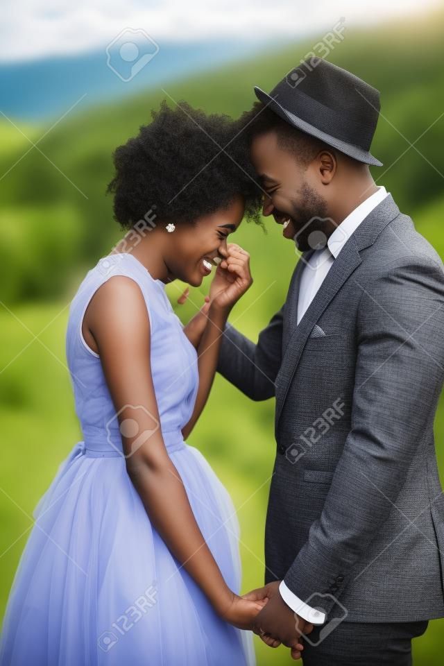 Black happy newlyweds hold hands, cheerful laugh and stand against beautiful landscape. Closeup.