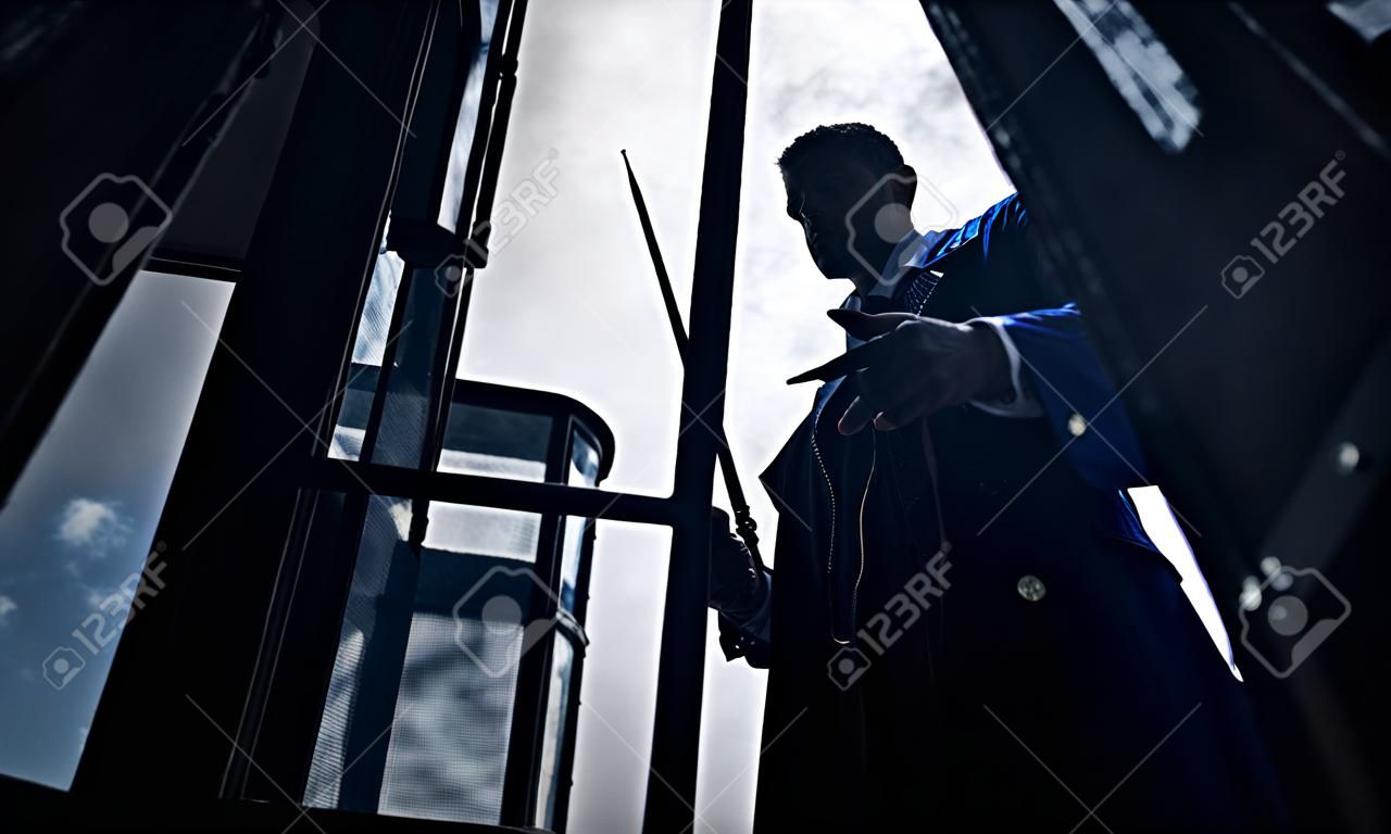 Silhouette of man in image of black magician with magic wand in his hand. Closeup.