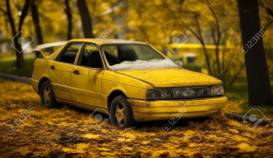 Old broken abandoned dark gray car on yellow leaves in the yard of an apartment building