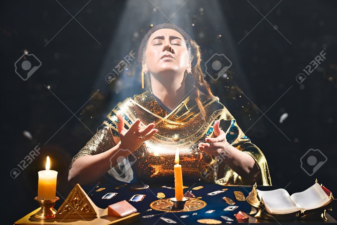 Astrology and divination. Portrait of a fortune teller who reads by candle, eyes closed in ecstasy. Black background. There are magic items on the table.