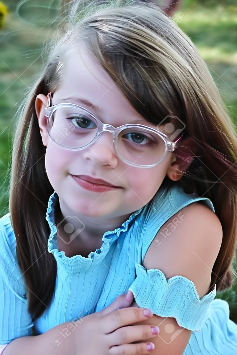 Kleine meid draagt een bril en kijkt direct naar de kijker. Ondiepe scherptediepte met selectieve focus op het gezicht van het kind.