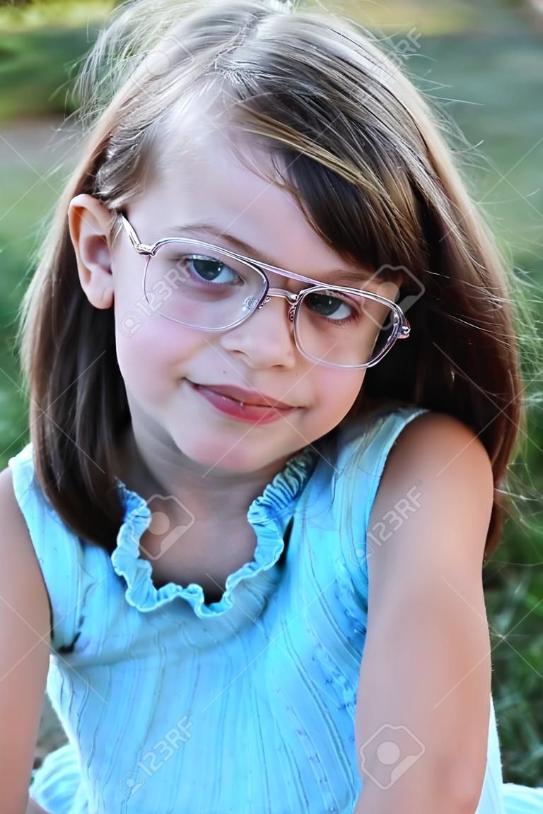 Kleine meid draagt een bril en kijkt direct naar de kijker. Ondiepe scherptediepte met selectieve focus op het gezicht van het kind.