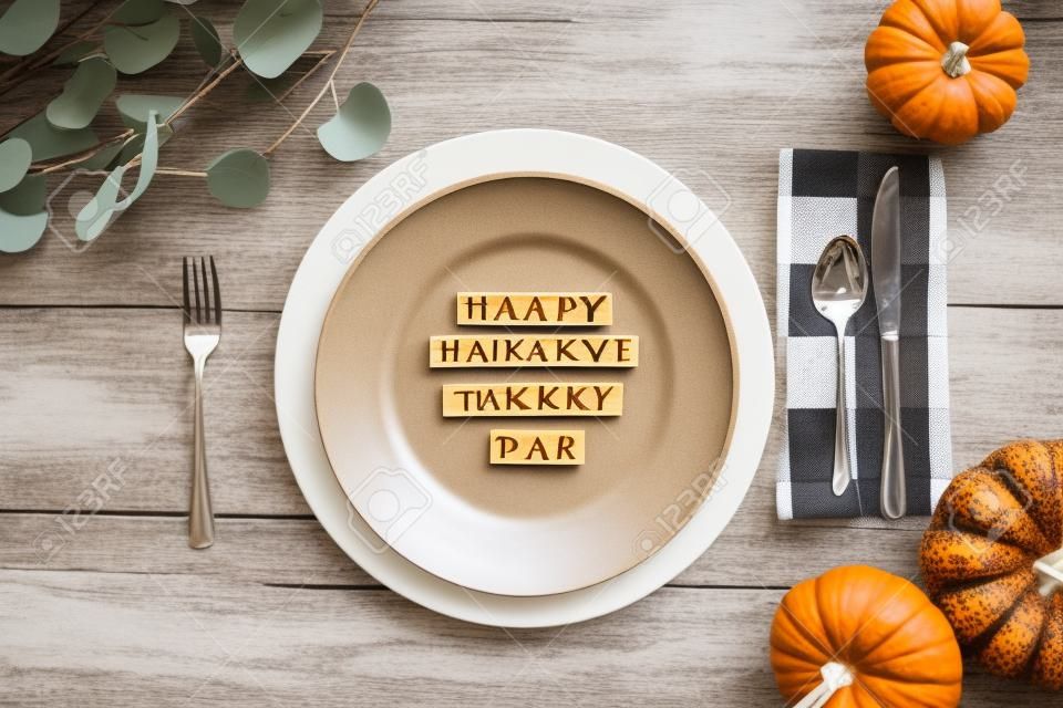 Thanksgiving place setting with plate, napkin, on a  decorated table shot from flat lay or top view position. Happy Friendsgiving Day spelled out with wood block letters.