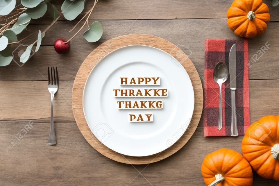 Thanksgiving place setting with plate, napkin, on a  decorated table shot from flat lay or top view position. Happy Friendsgiving Day spelled out with wood block letters.