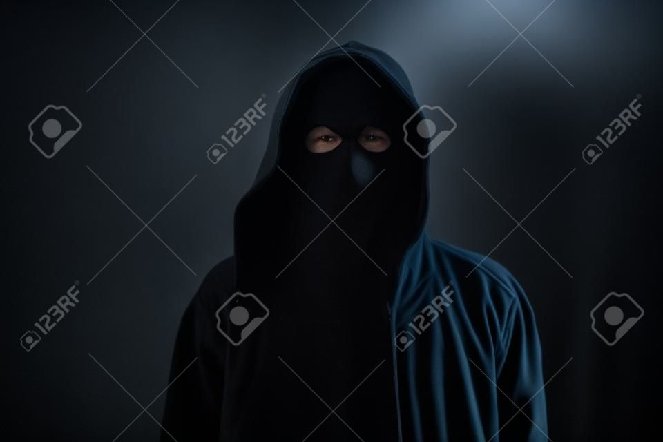 Homem sem rosto desconhecido e irreconhecível sem identidade vestindo capuz no quarto escuro, pessoa criminosa assustadora.