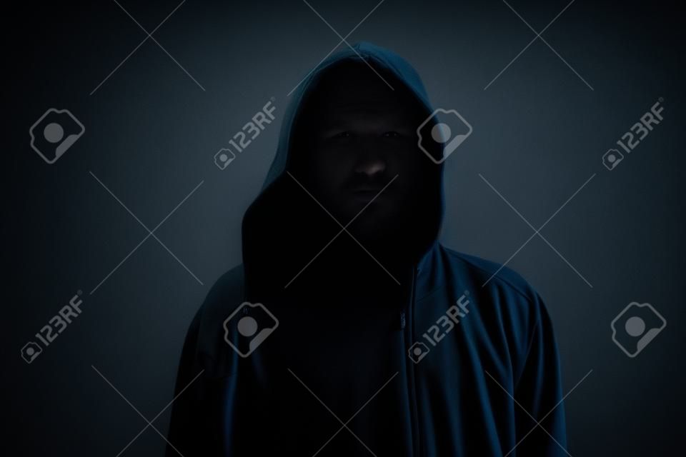 Faceless unknown and unrecognizable man withouth identity wearing hood in dark room, spooky criminal person.