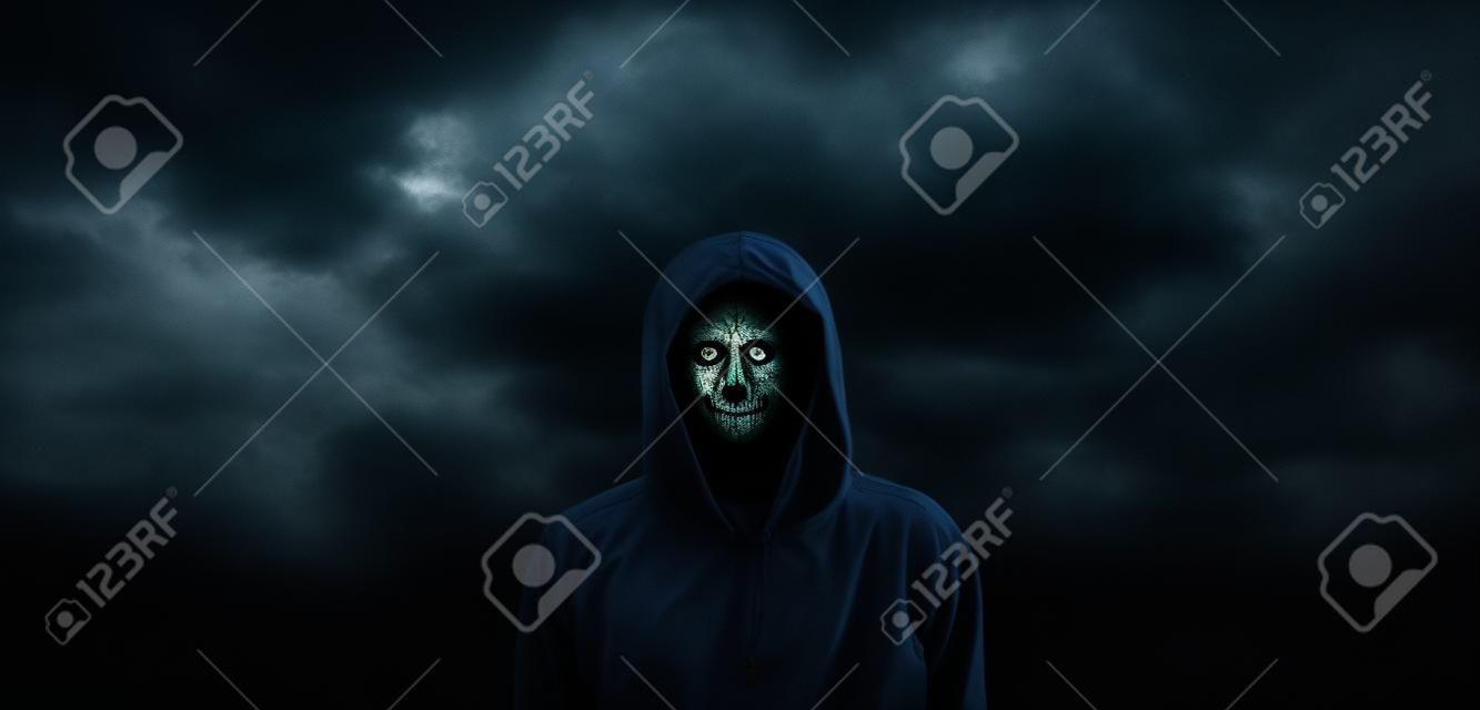 Spooky hooded person with obscured face against the dark dramatic sky