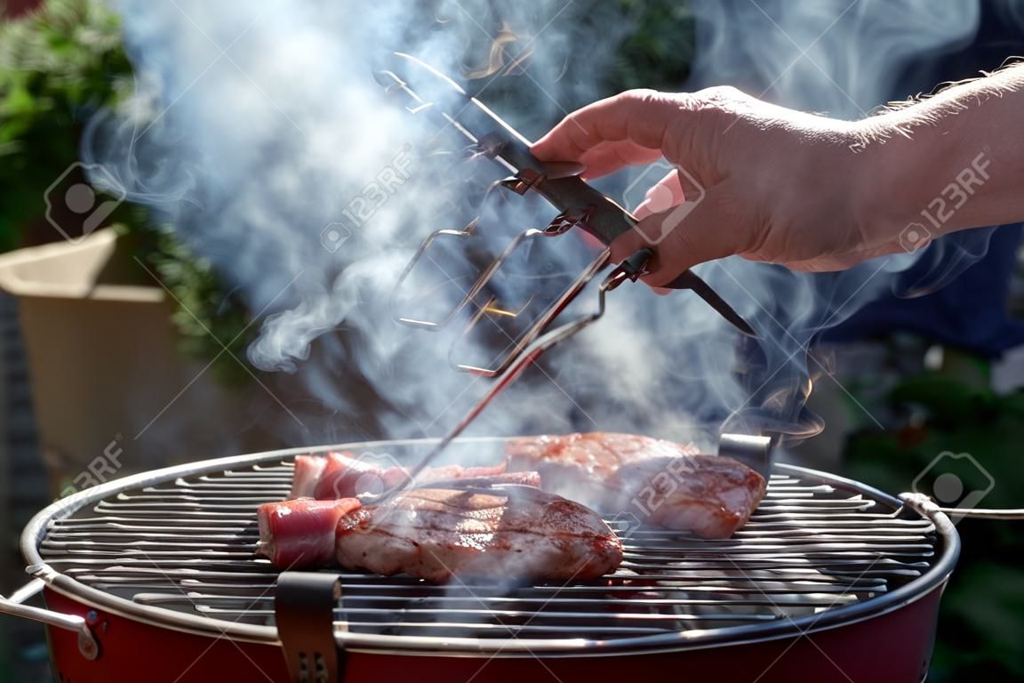 Hand turns marinated grill, which lies on a grate of a smoking grill.