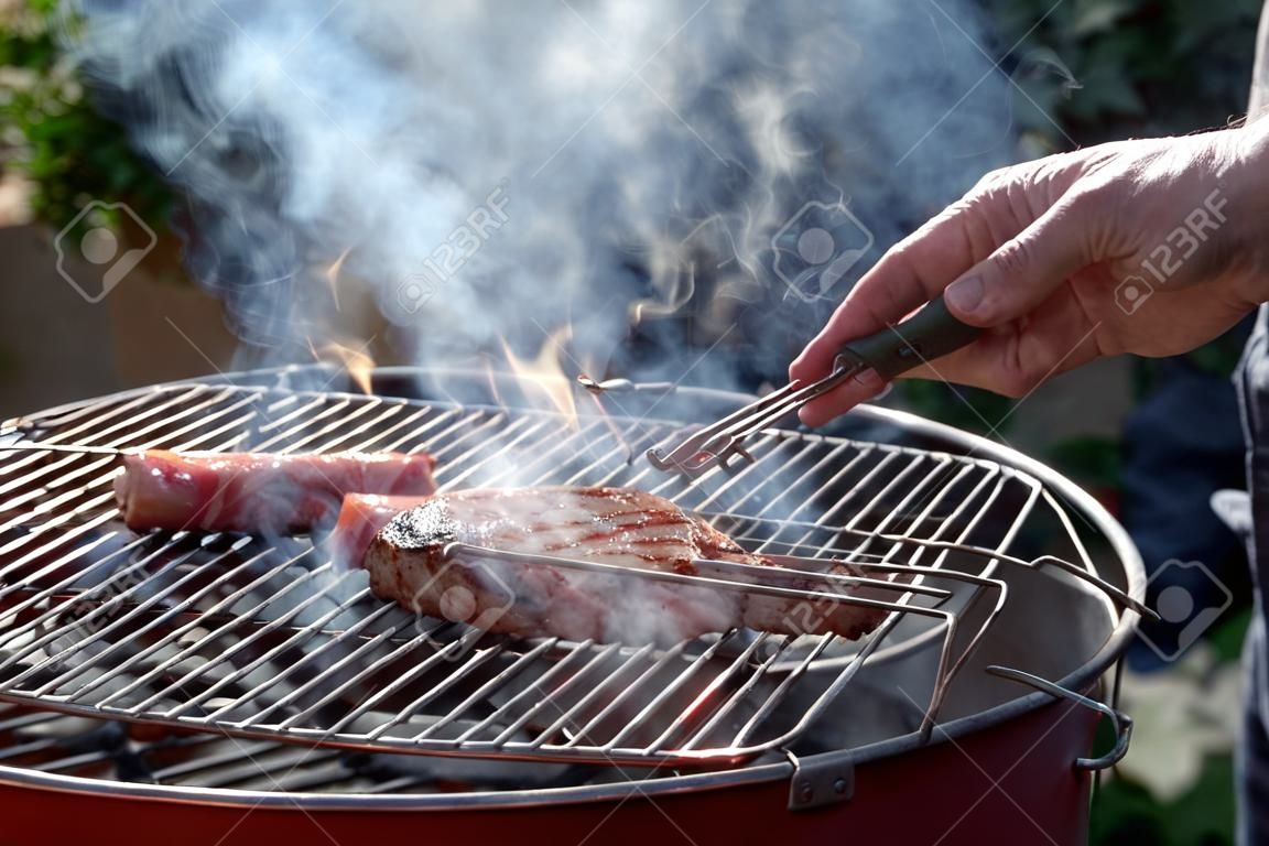 Hand turns marinated grill, which lies on a grate of a smoking grill.