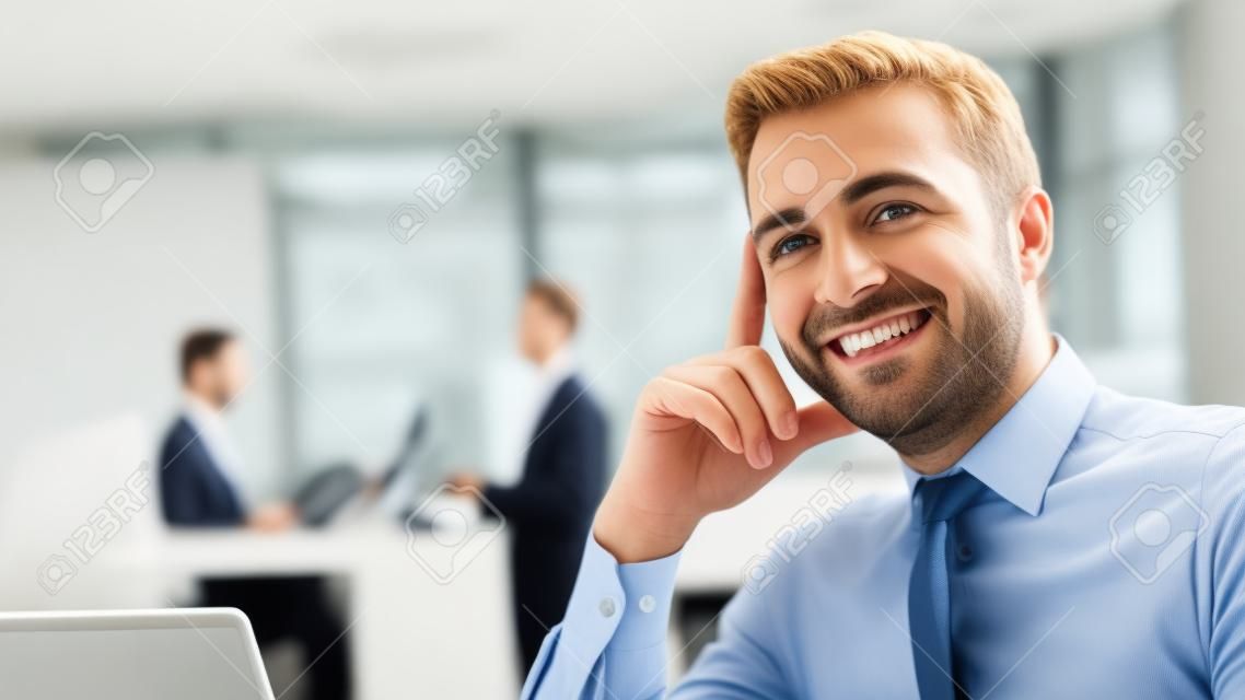 자신감이 생긴 사업가 사무실 책상에 앉아 배경에 서 카메라, 사무실 인테리어 및 비즈니스 사람들이 미소를 선택적 포커스